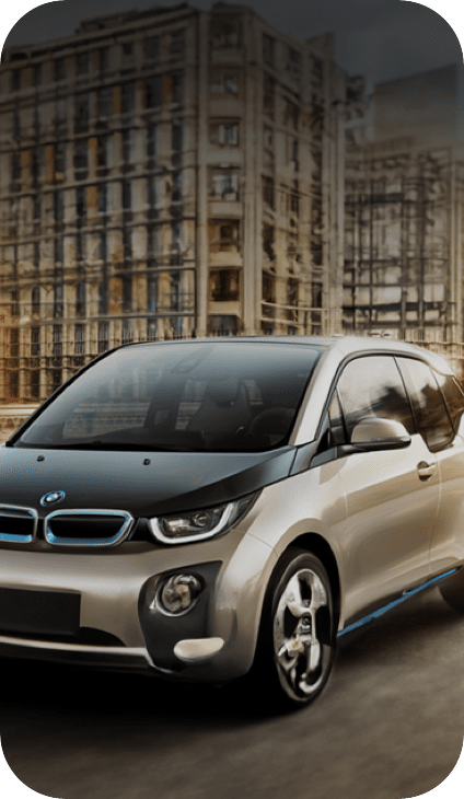 都市の背景を背に、銀色のBMW電気自動車が市街地の道路を走行している画像。