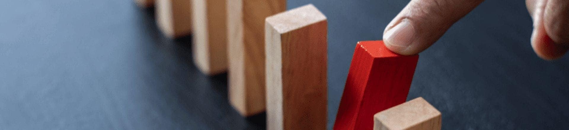 A row of wooden blocks are lined up like dominoes, with a finger blocking a red block.
