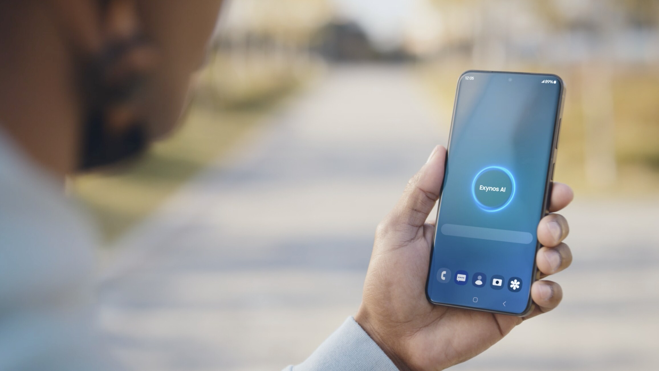 A person holding a smartphone with a voice assistant interface active on the screen, standing outdoors on a sunlit pathway.
